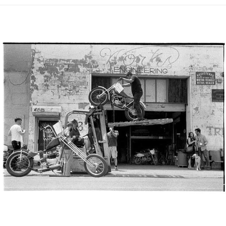 A black and white image of a motorbike being lifted by a forklift truck outside the New York City Motorcycles showroom.