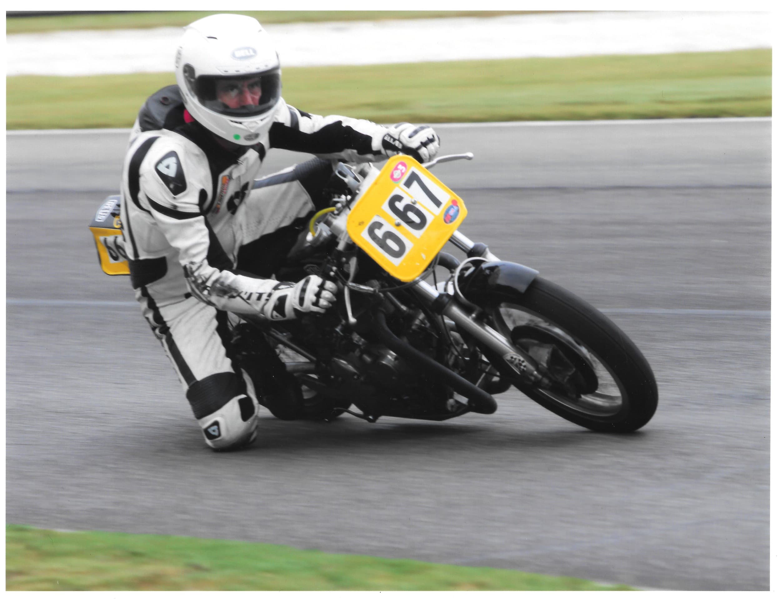 An image of Larry from New York City Motorcycles racing on a white coloured vintage motorcycle with the race number 667 on the front. He's leaning low into a corner.