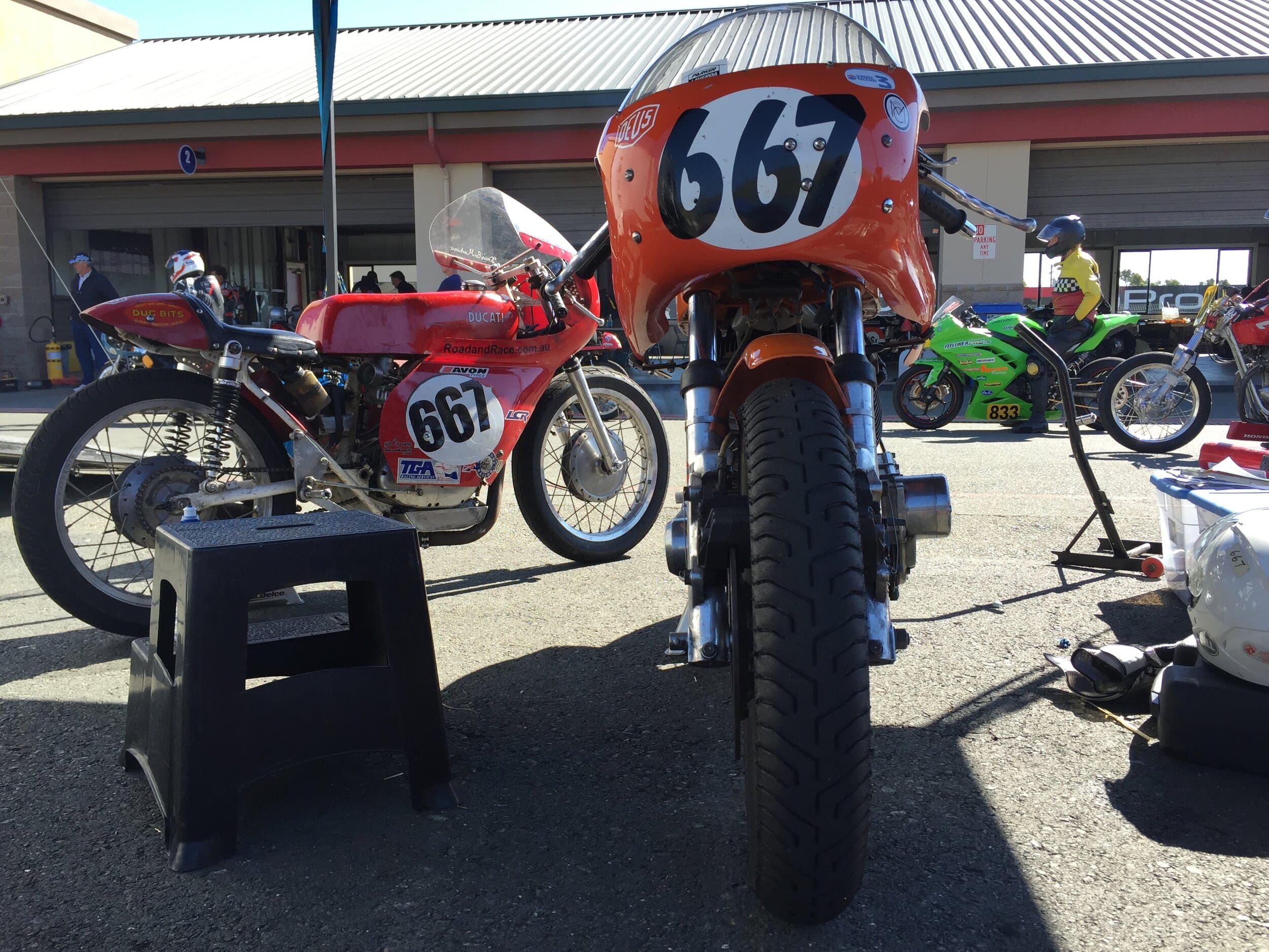 An orange Laverda and a red Ducati vintage motorbikes basking in the sunlight in the pit on race day.