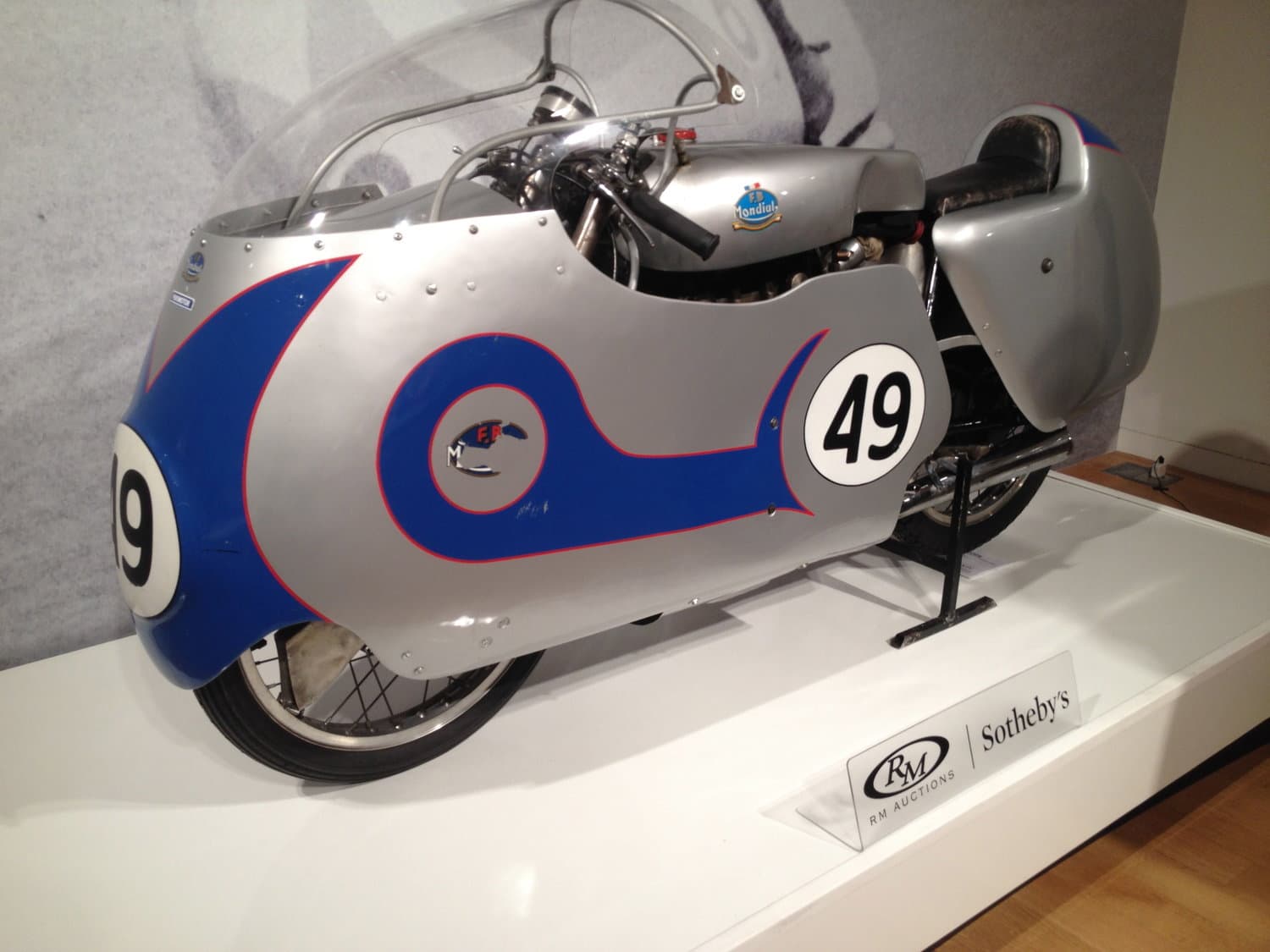 A photograph of a silver coloured vintage motorcycle being displayed in Sotheby's auction house.